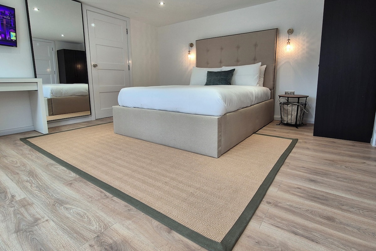 A modern bedroom with a large bed, a desk, and a mirror.