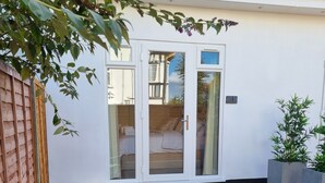 A patio with outdoor seating, a bed visible through glass doors, and a wooden fence. - Hotel CG London (London)