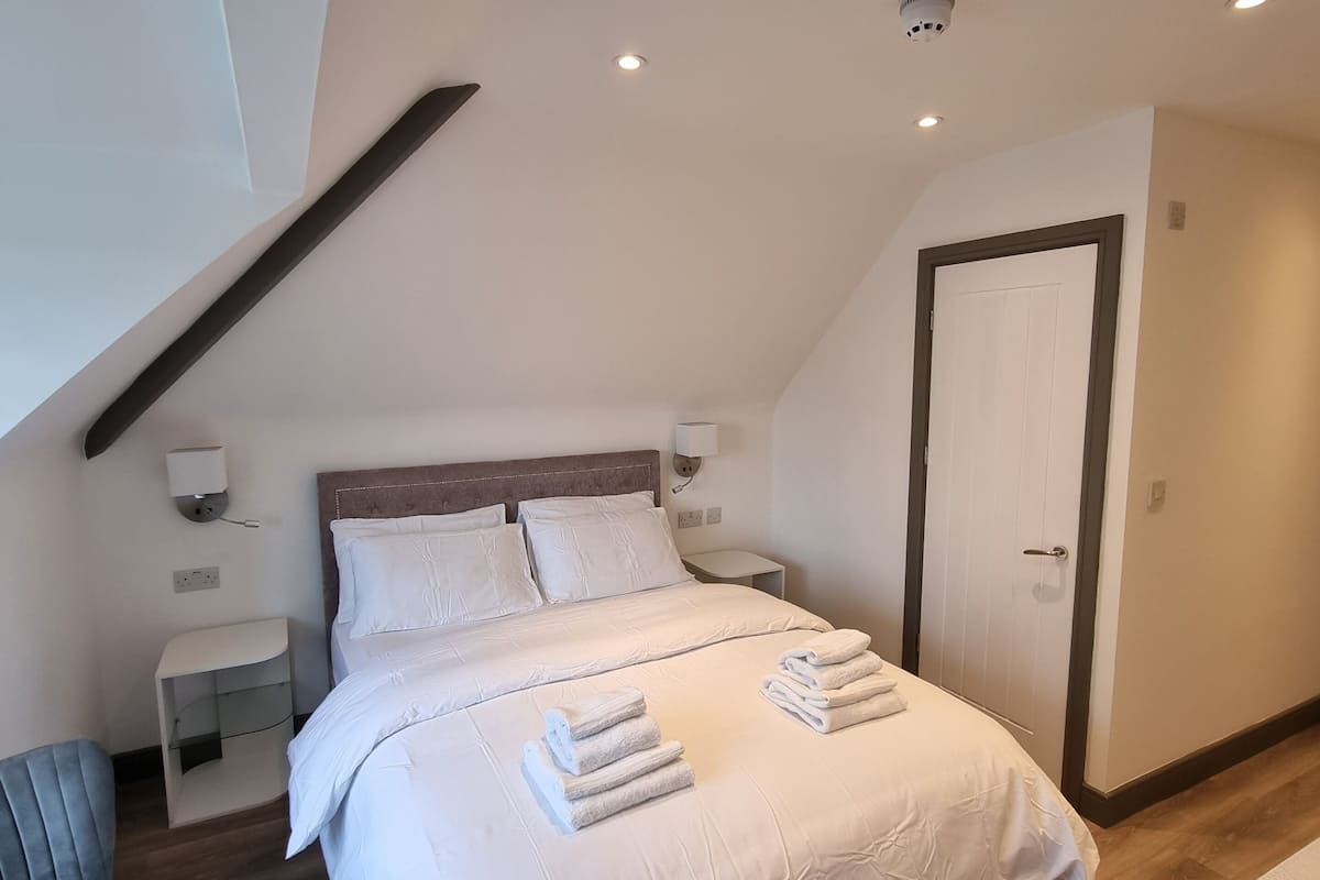 A modern bedroom with a bed, nightstands, a chair, and a door.