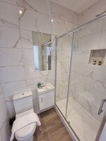Un baño moderno con ducha acristalada, inodoro blanco y tocador con espejo.