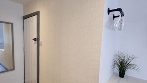 A hallway with a wooden floor, a white textured wall, a door, a mirror, a wall-mounted towel rack, and a potted plant. - Hotel CG London (London)