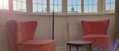 A room with two pink chairs, a small table, a patterned rug, and a floor lamp.