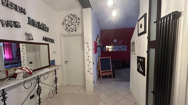 A hotel lobby with a reception desk, a mirror, a chalkboard with a welcome message, and a red accent wall. - Charming apartment in Parma (Parma)