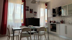 A compact kitchen with white cabinets, a dining table with chairs, and a hanging light fixture. - Charming apartment in Parma (Parma)