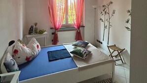 A small, well-lit bedroom with a single bed, a bedside table, a lamp, and a window with sheer curtains. - Charming apartment in Parma (Parma)