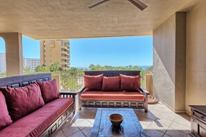 A balcony with a sofa and a table, overlooking a cityscape and the sea.