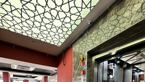 Un interior con suelo de mármol, puerta de ascensor de vidrio y diseño geométrico en el techo.