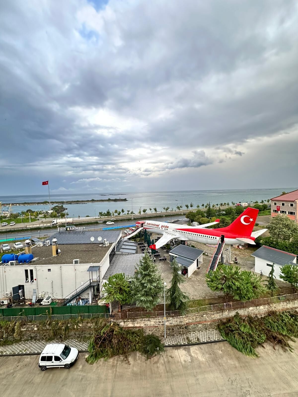 An airport terminal with a red and white airplane parked outside, surrounded by buildings and a road.
