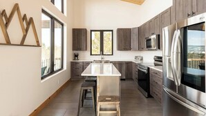 Une cuisine moderne dotée d’un îlot central, d’appareils électroménagers en acier inoxydable et offrant une vue sur l’extérieur.