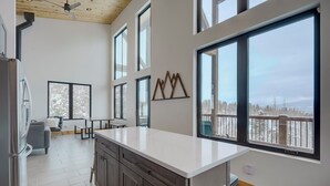 Une cuisine moderne dotée d’un grand îlot central, de meubles en bois et offrant une vue sur un paysage enneigé grâce à de grandes fenêtres.