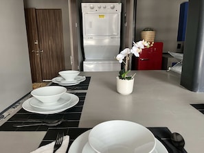 A kitchen with a white refrigerator, a red cabinet, and a dining table set with white plates, bowls, and cutlery.