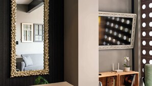 A room with a large mirror, a wall-mounted TV, and a small plant on a wooden shelf.