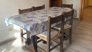 Una taula de menjador amb un mantell floral, cadires de fusta i un quadre amb marc a la paret.