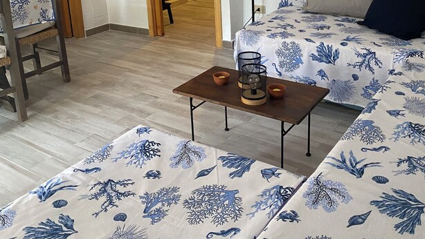 Una habitació amb un llit, una cadira, una taula amb safates, una làmpada i un mapa penjat a la paret.