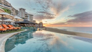 Zona de piscina con sillones de descanso y vistas a la playa y al atardecer.