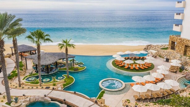 Un resort con zona de piscina, sillas de descanso y vista al mar.