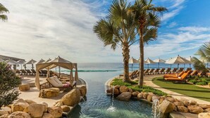 Un área de piscina en un resort con sillas de descanso, una palmera y vista despejada del océano.
