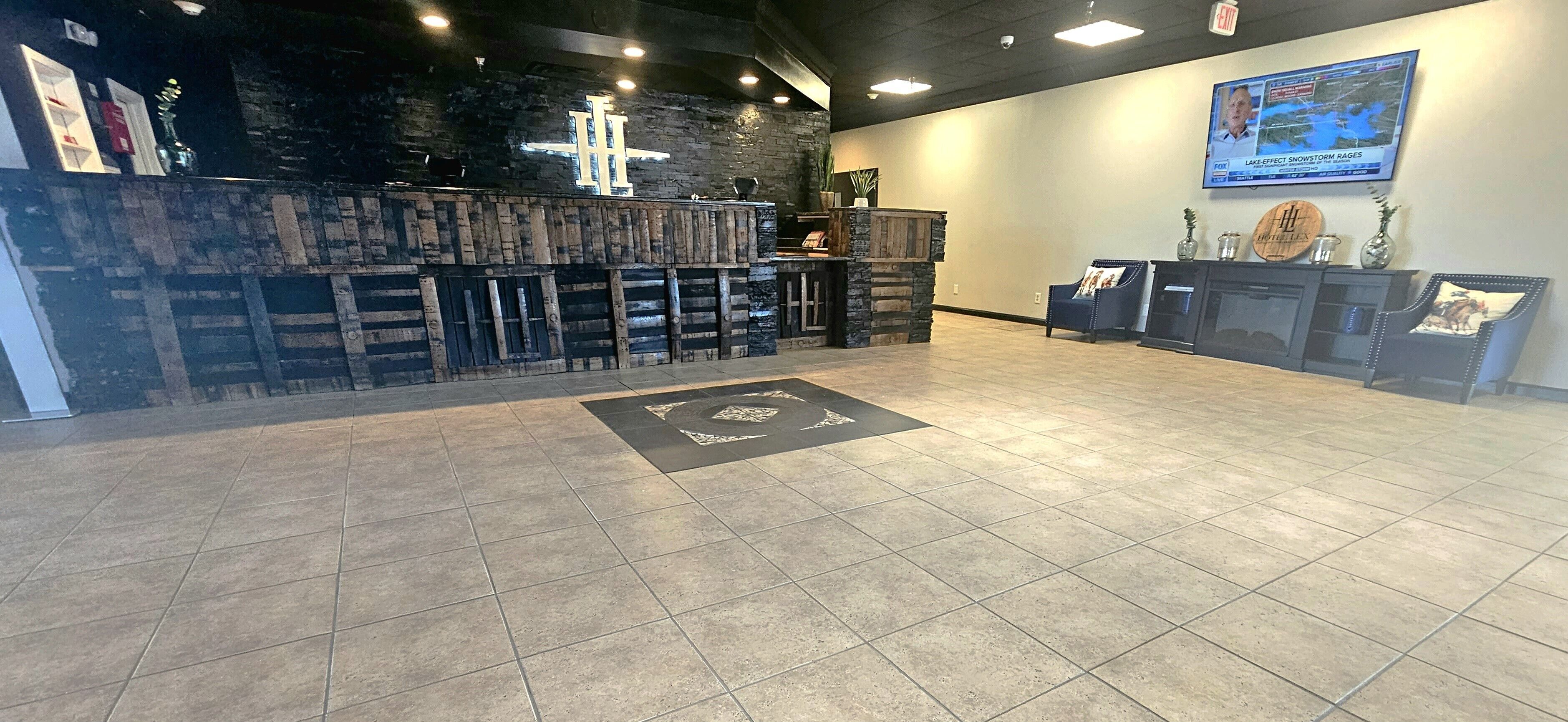 A reception area with a stone wall, a wooden reception desk, a tiled floor, and a mounted TV displaying a news channel.