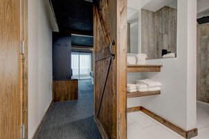 Un baño moderno con puerta de madera, zona de ducha y estante empotrado con toallas.