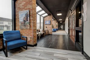 A spacious hallway with a brick wall, a large window, and a blue chair.