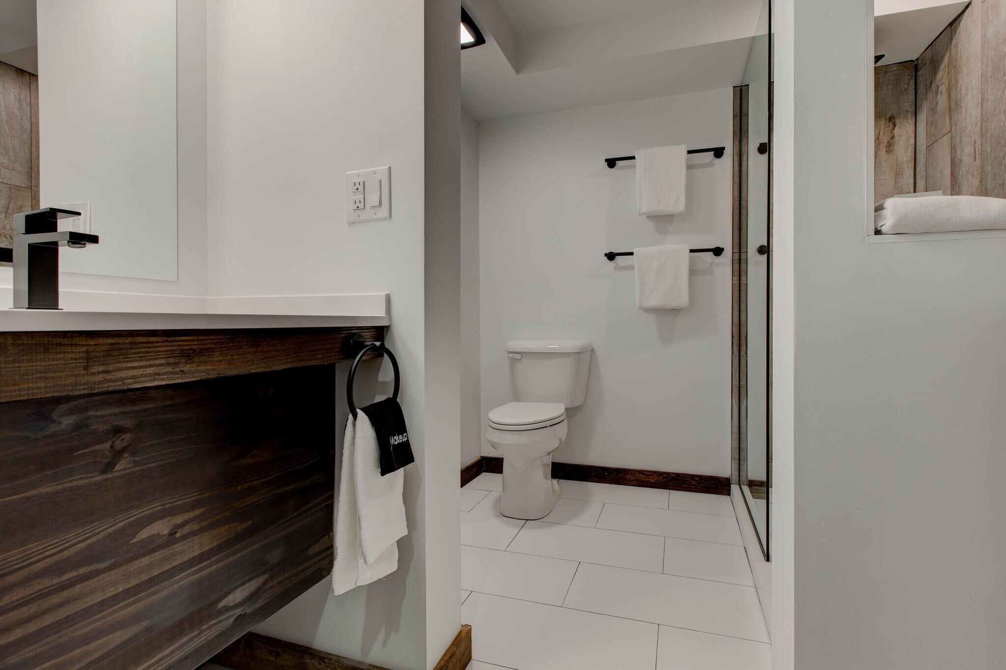 A modern bathroom with a white toilet, a shower area, and a wooden vanity with a towel rack.