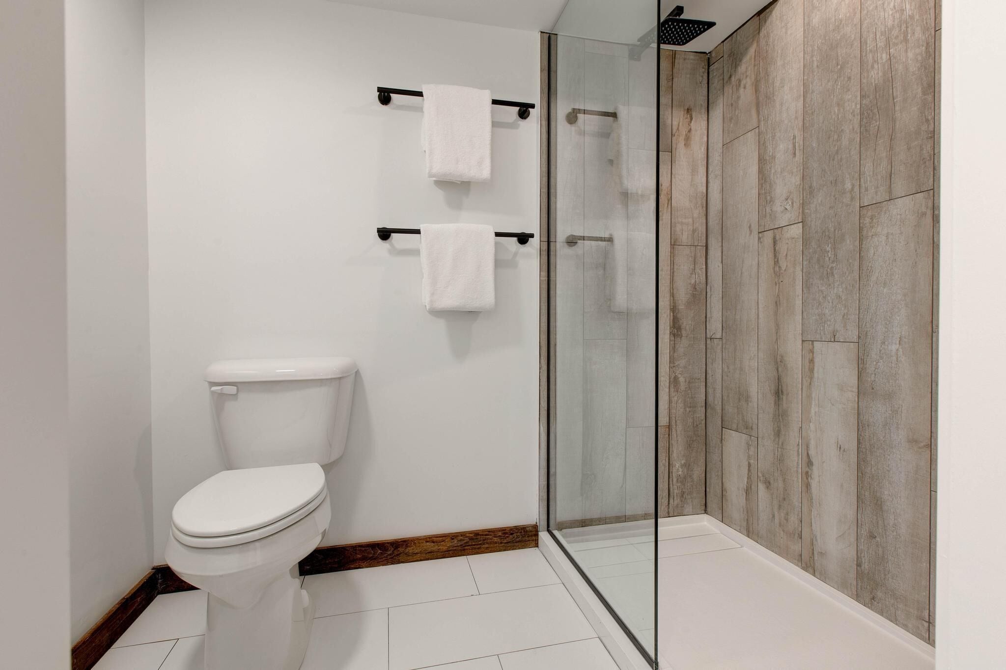 Une salle de bain moderne avec une douche à parois de verre, des carreaux blancs et un mur d’accent en bois.