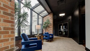 A modern lobby with blue chairs, a brick wall, and a large window. - Hotel Lex and Conference Center, Trademark Collection (Lexington)
