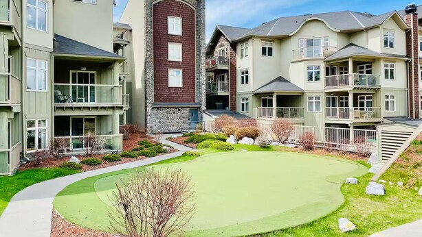 A residential complex with multiple two-story buildings, a central courtyard with a green lawn, and a small pond. - A Lovely Studio with Full Kitchen & AC (Canmore)