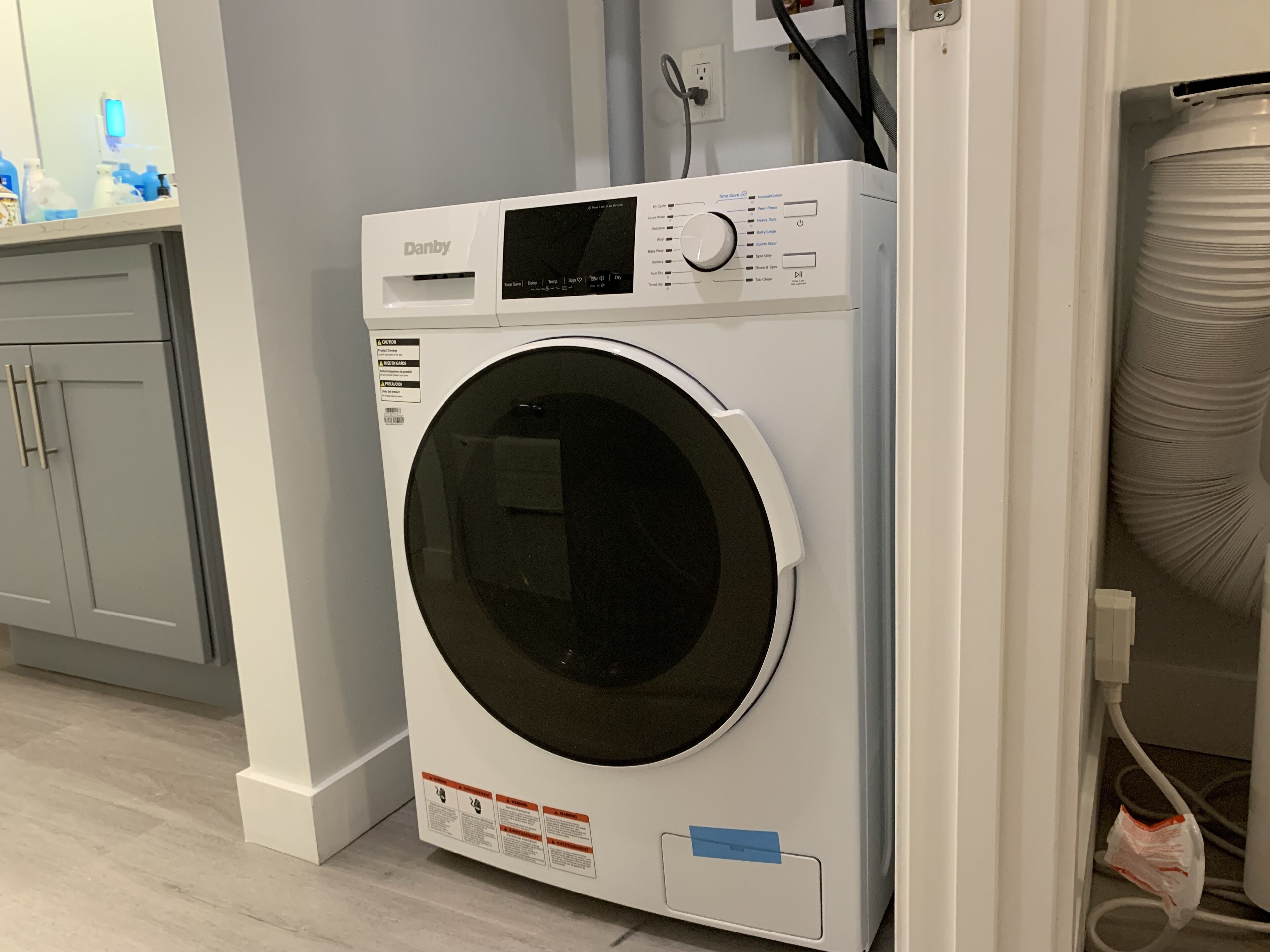 Een witte Danby wasmachine met voorlaadopening in een moderne keuken met grijze kastjes en een wit aanrecht.