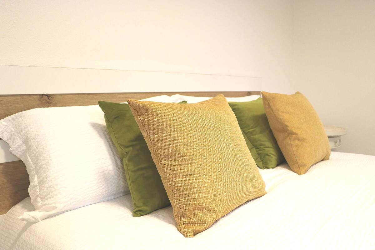 A bed with white bedding and three pillows in different colors.