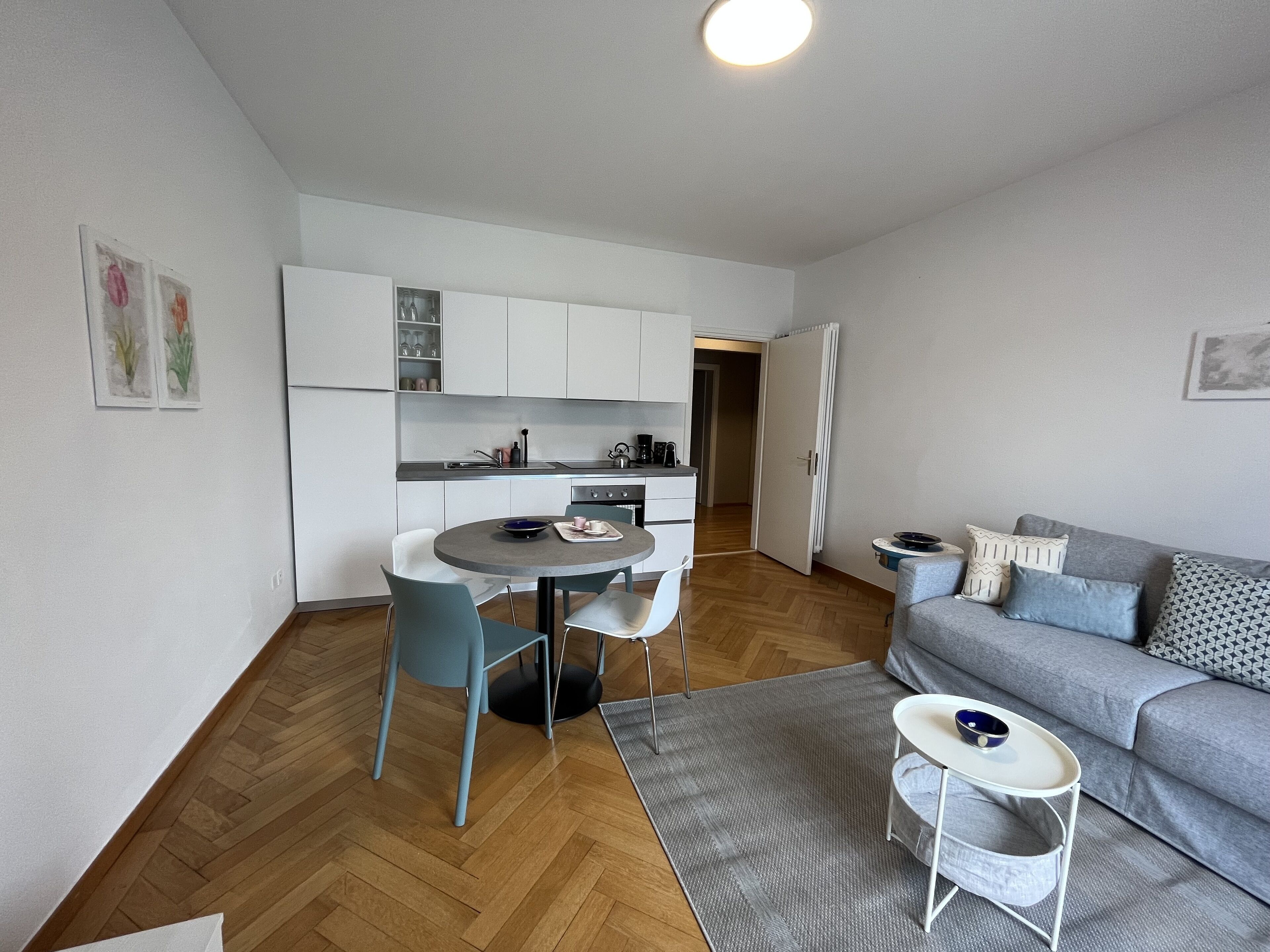 Un espacio habitable compacto con kitchenette, comedor y zona de estar con sofá y mesita auxiliar.