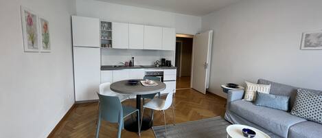 Un espacio habitable compacto con kitchenette, comedor y zona de estar con sofá y mesita auxiliar.