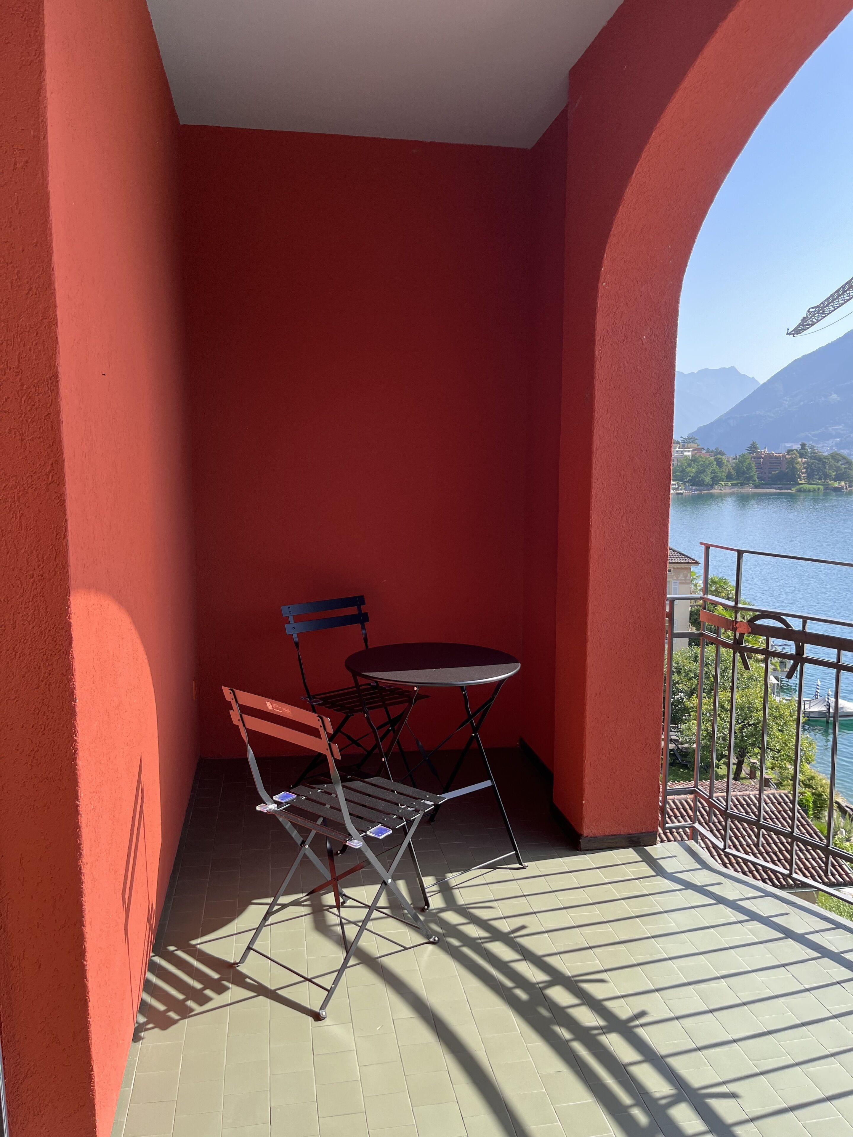 A balcony with a red wall, a metal table, and two chairs.