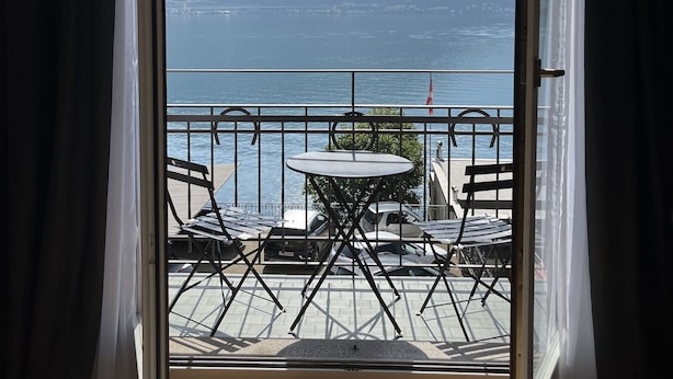 A balcony with a table and chairs, overlooking a lake and mountains. - 76thelakehouse (Melide)