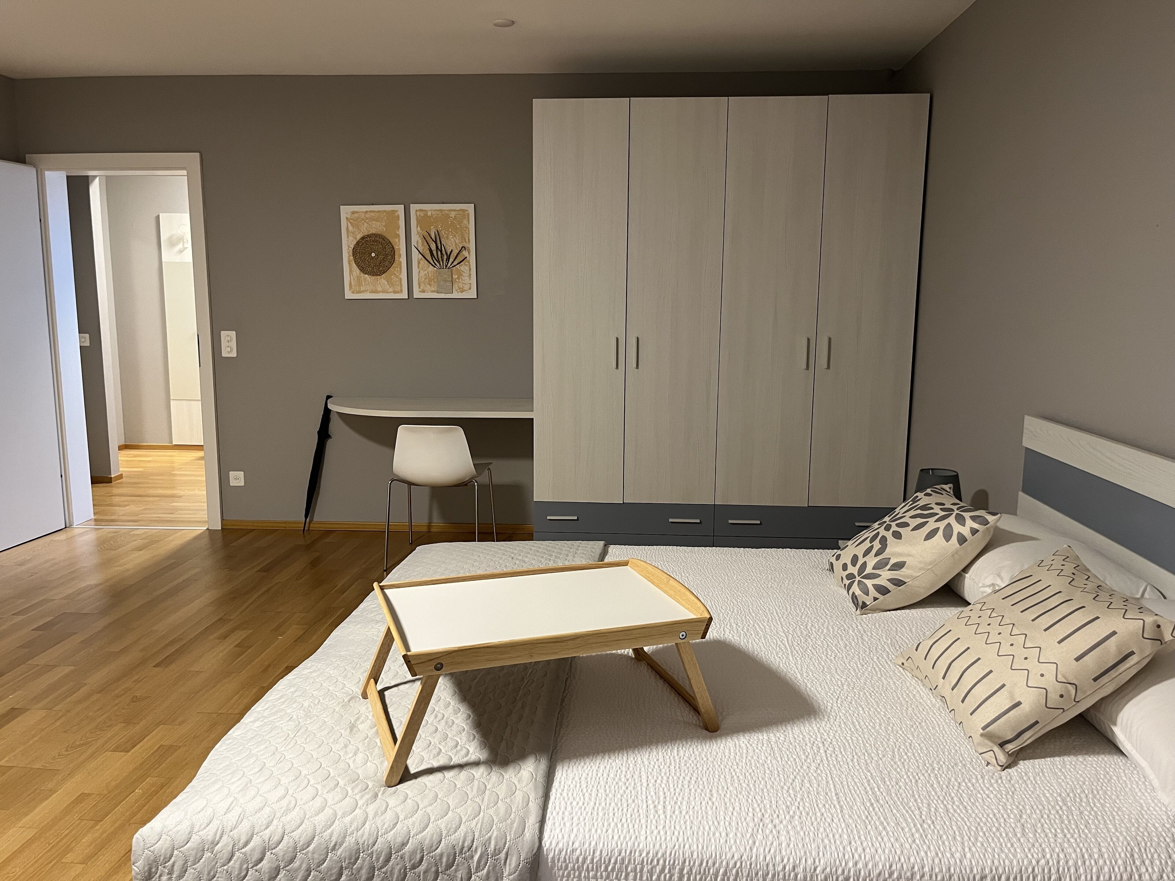 Un dormitorio con cama, mesita de noche, armario, escritorio, silla y dos obras de arte en la pared.