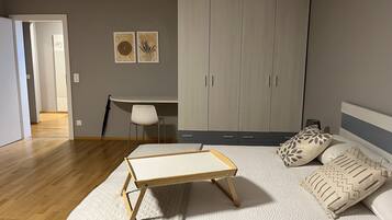 Un dormitorio con cama, mesita de noche, armario, escritorio, silla y dos obras de arte en la pared.