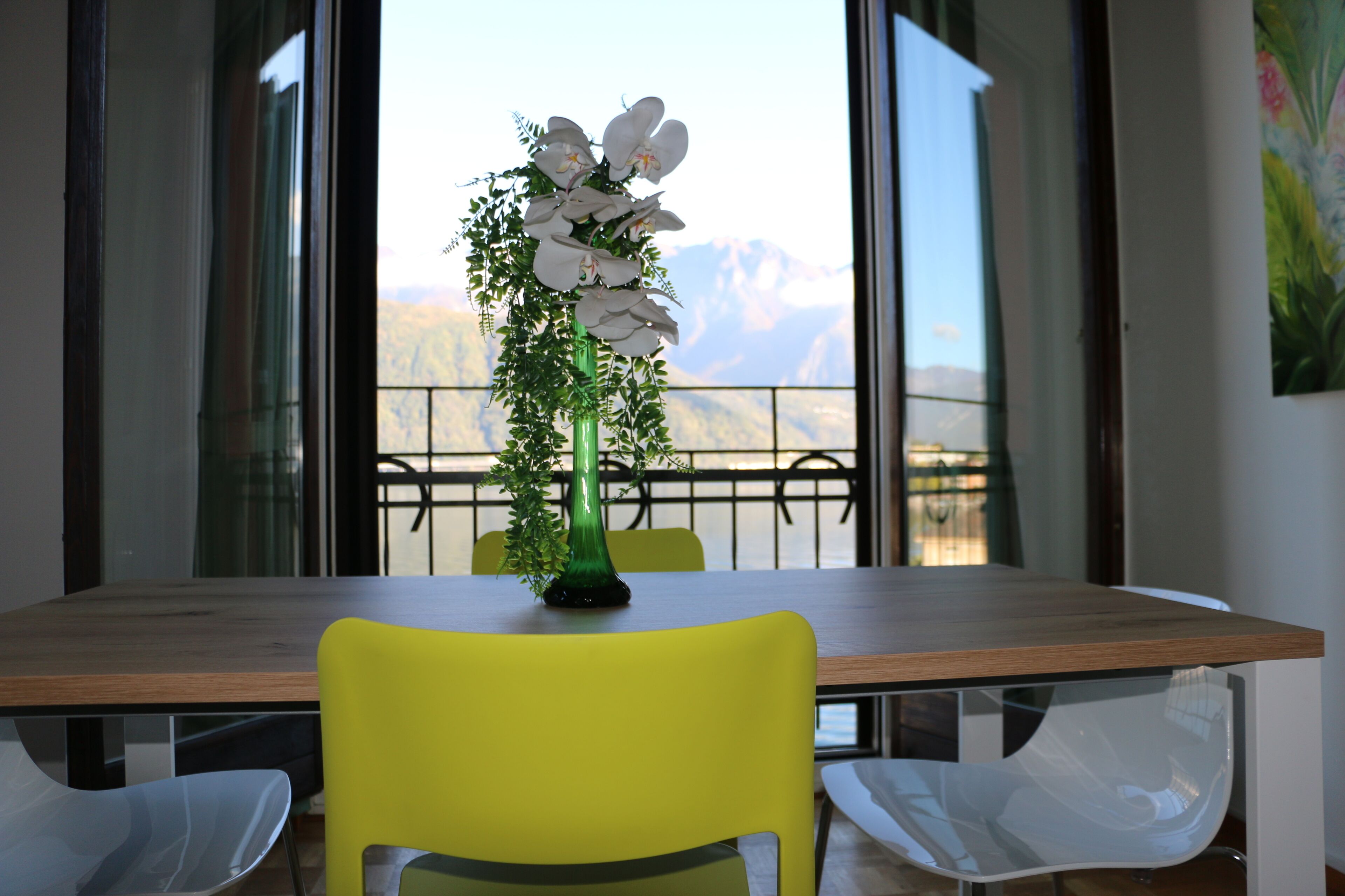 Zona pranzo con un tavolo in legno, una sedia gialla e un vaso verde con fiori bianchi.