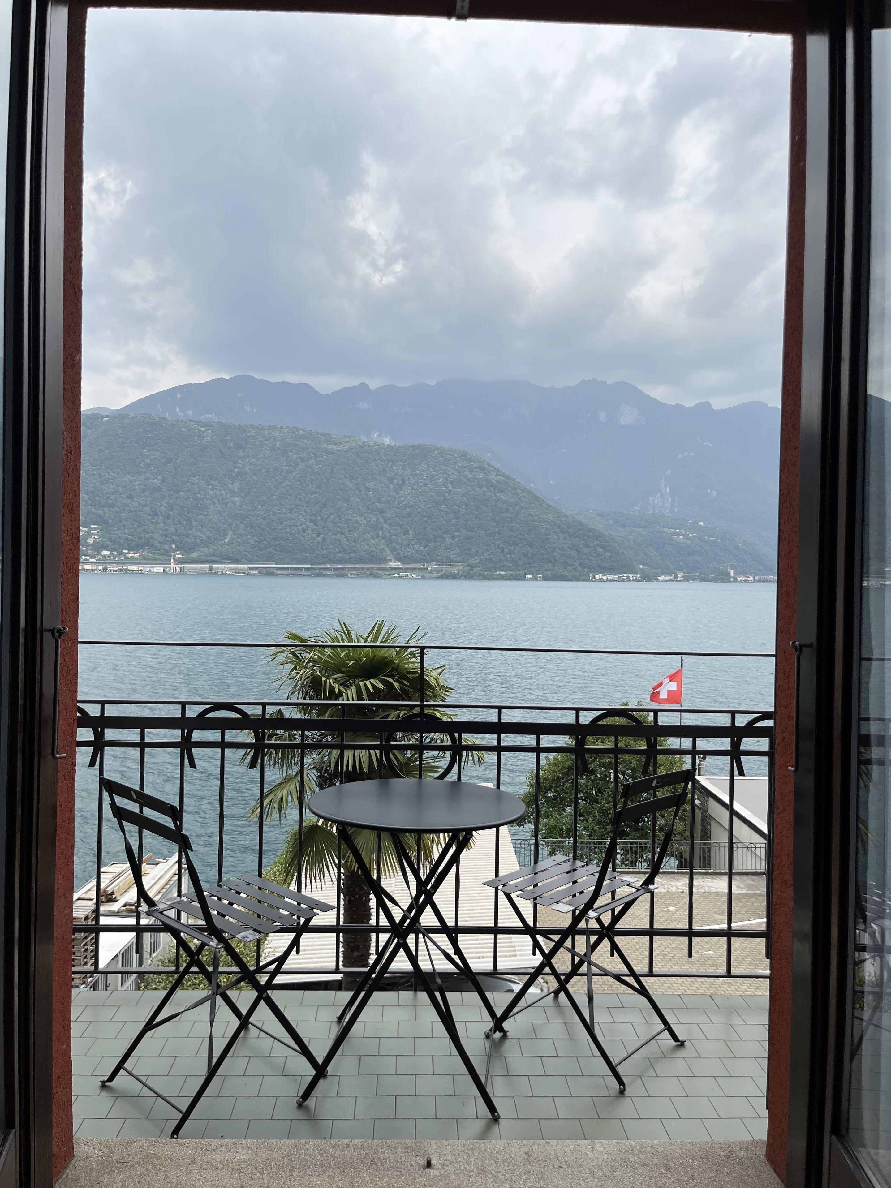 A balcony with a table and chairs, overlooking a body of water and mountains.