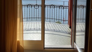 A room with a large sliding glass door leading to a balcony with a metal railing, overlooking a body of water and distant mountains. - 76thelakehouse (Melide)