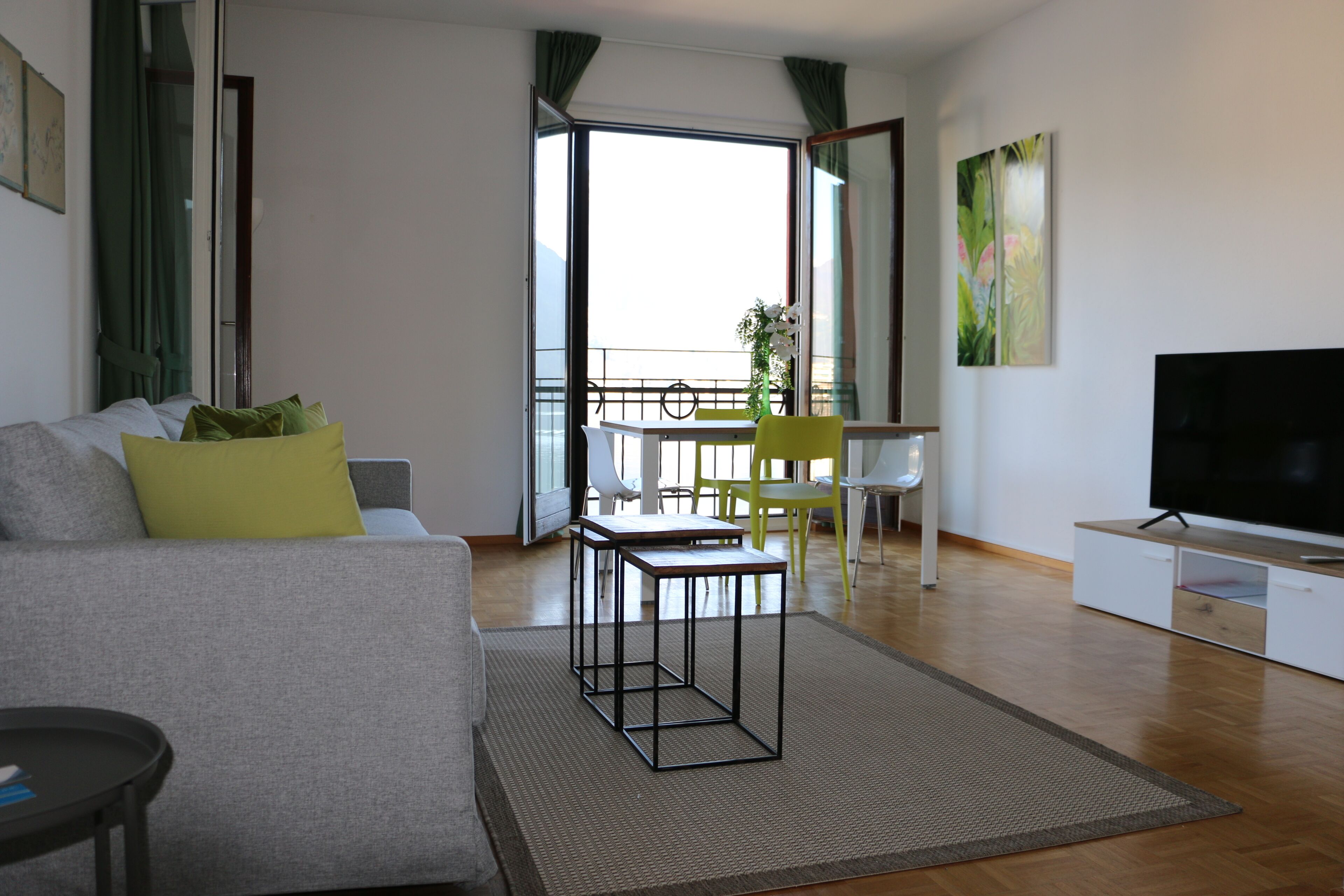 A modern living room with a sofa, a coffee table, a TV, and a balcony with a dining area.