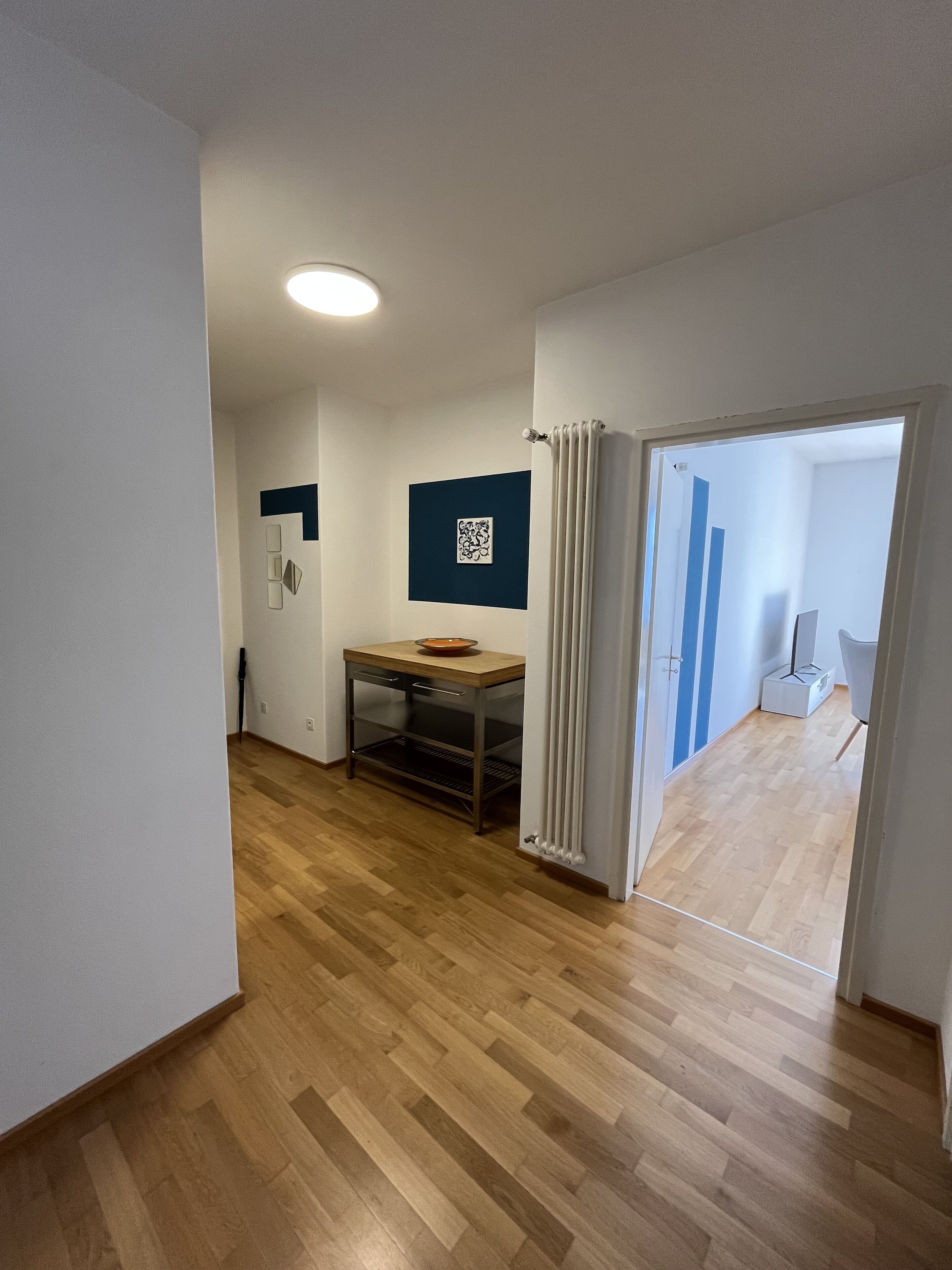Ein Zimmer mit Holzboden, einem Tisch mit einer Schüssel, einem Heizkörper und einer Tür zu einem anderen Raum.