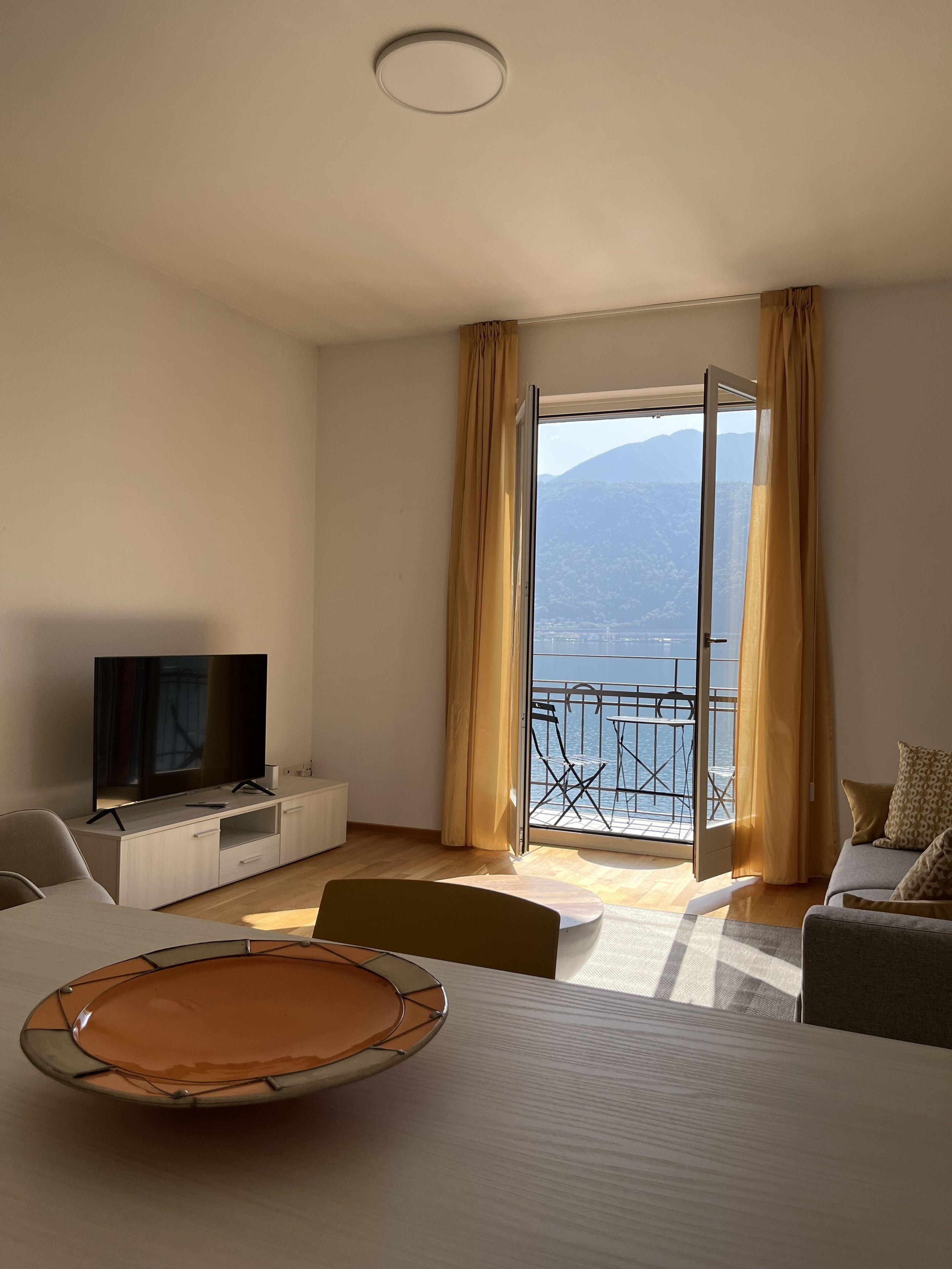 A hotel room with a TV, a dining table, a sofa, and a balcony with a view of the sea.