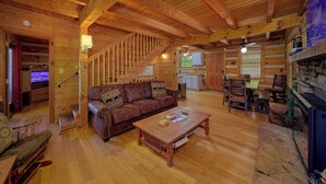 Interno di una baita in legno con divano, tavolino, tavolo da pranzo, sedie, camino e angolo cottura.