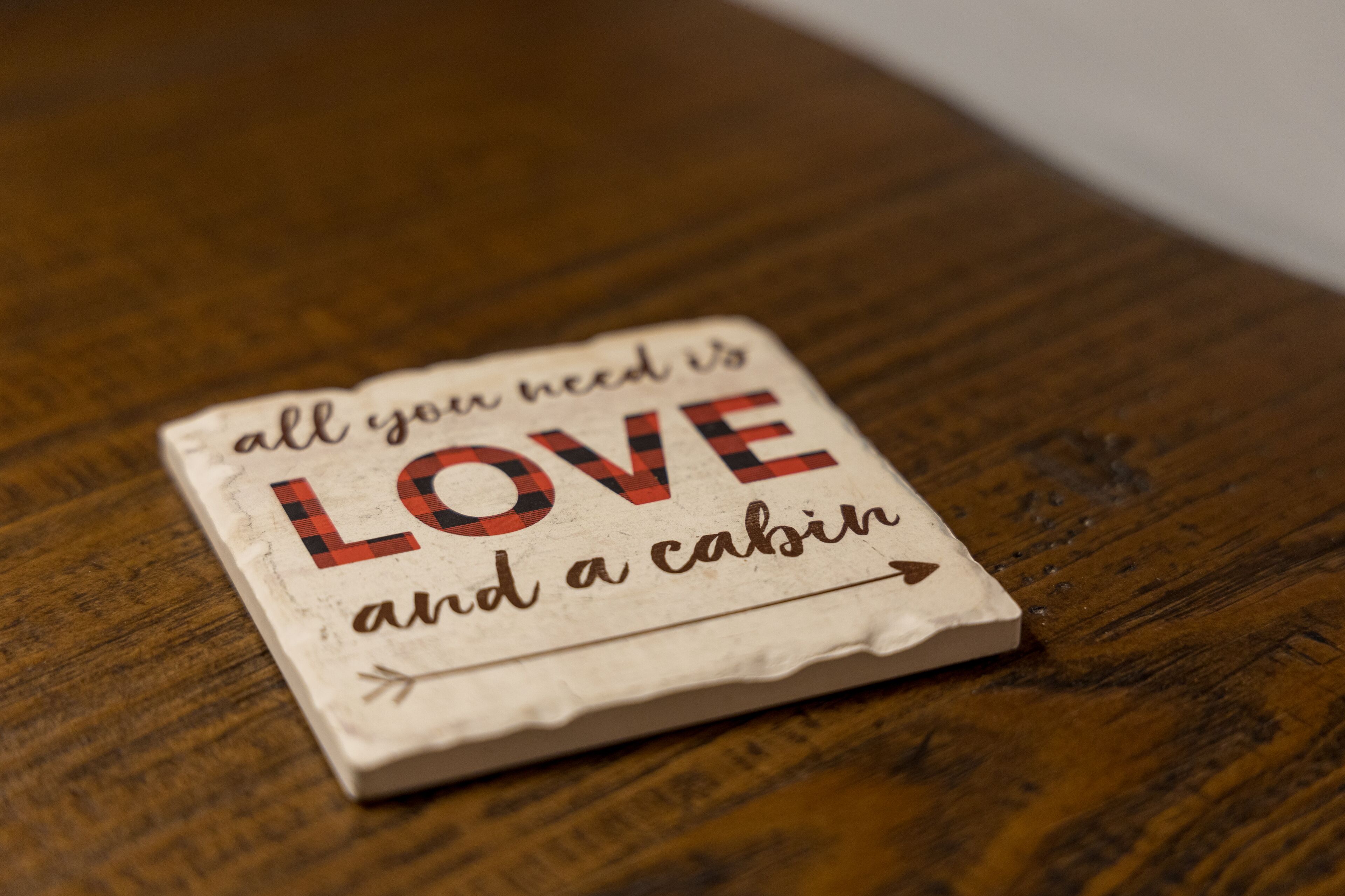 A wooden table with a small, rectangular object on it. The object has text that reads "all you need is LOVE and a cabin."