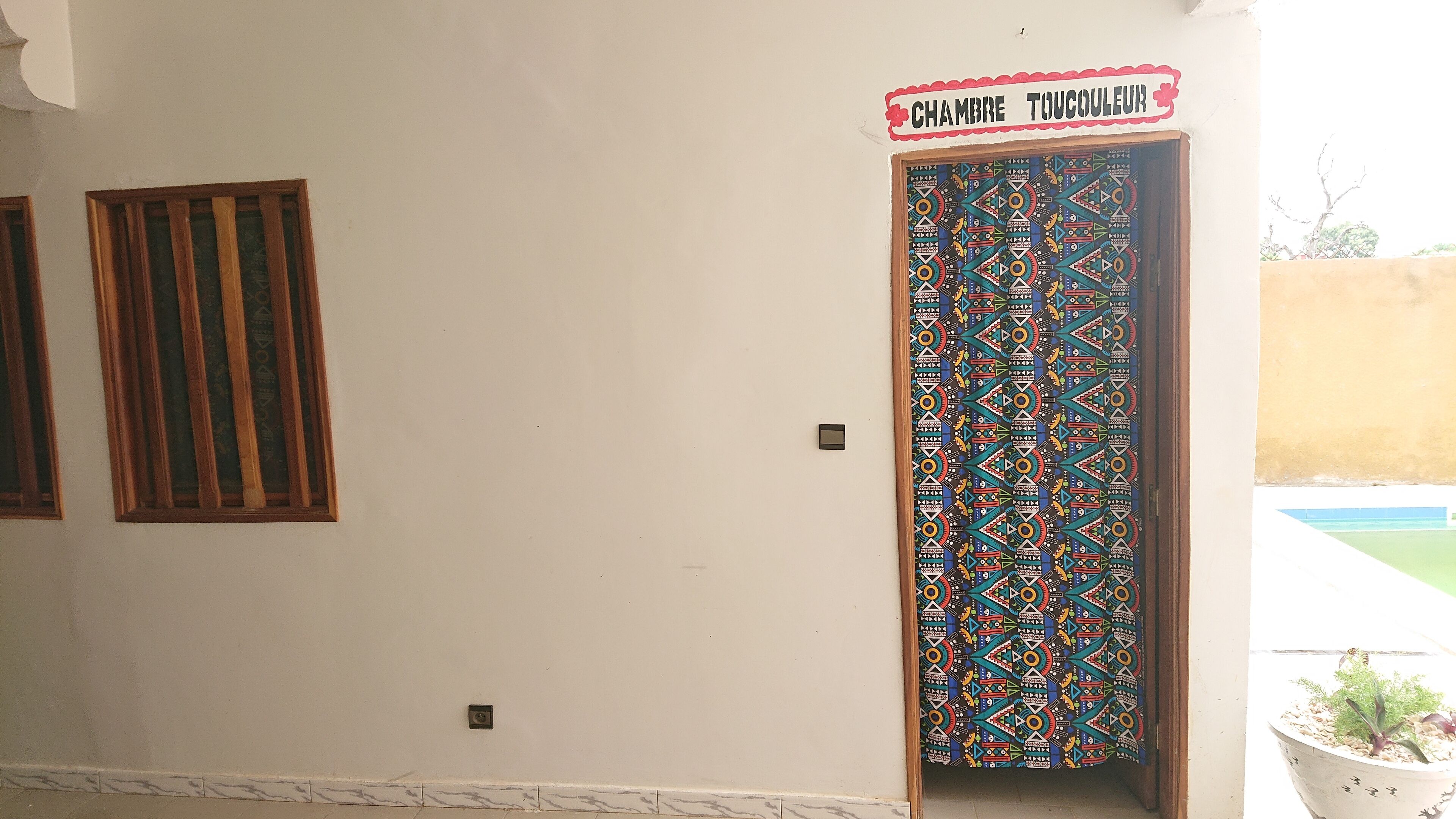 A door with a colorful geometric pattern, a small sign above it, and a potted plant to the right.