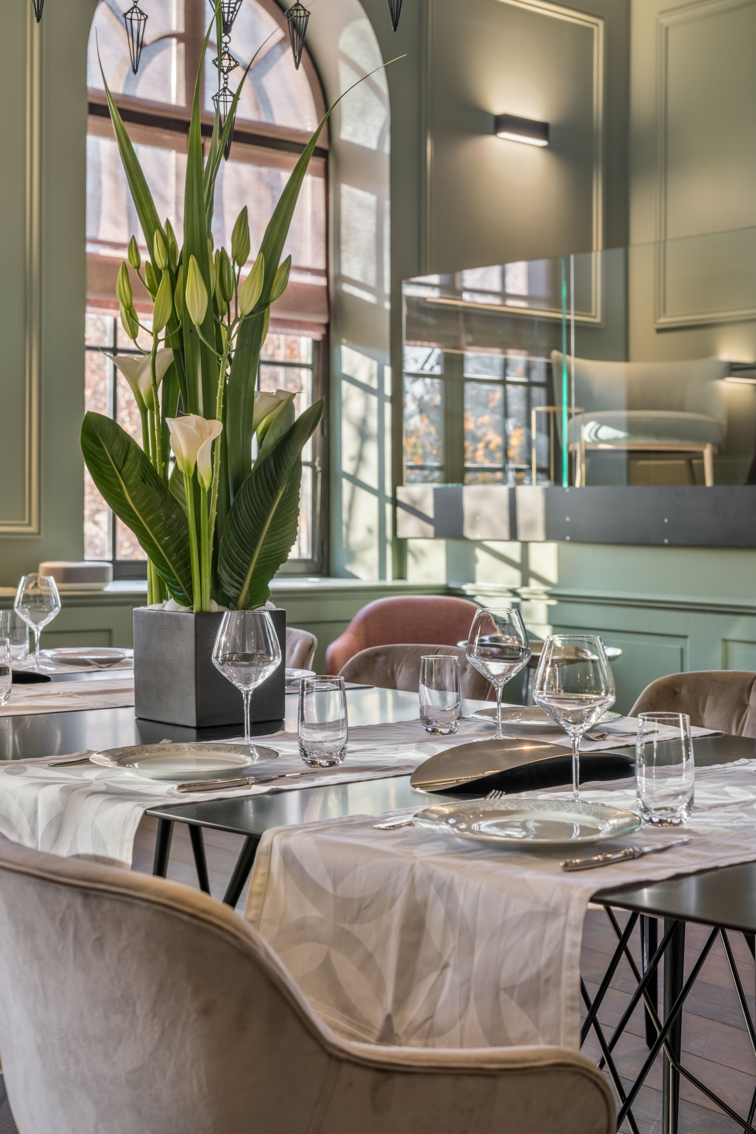 A dining table set with plates, cutlery, and wine glasses, surrounded by chairs.