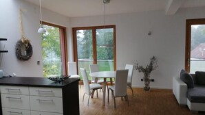 Un soggiorno moderno con zona pranzo, pavimento in legno, un divano bianco e cucina con piano di lavoro nero.