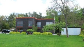 Un edificio moderno a due piani con tetto rosso, immerso in un prato curato e qualche albero.