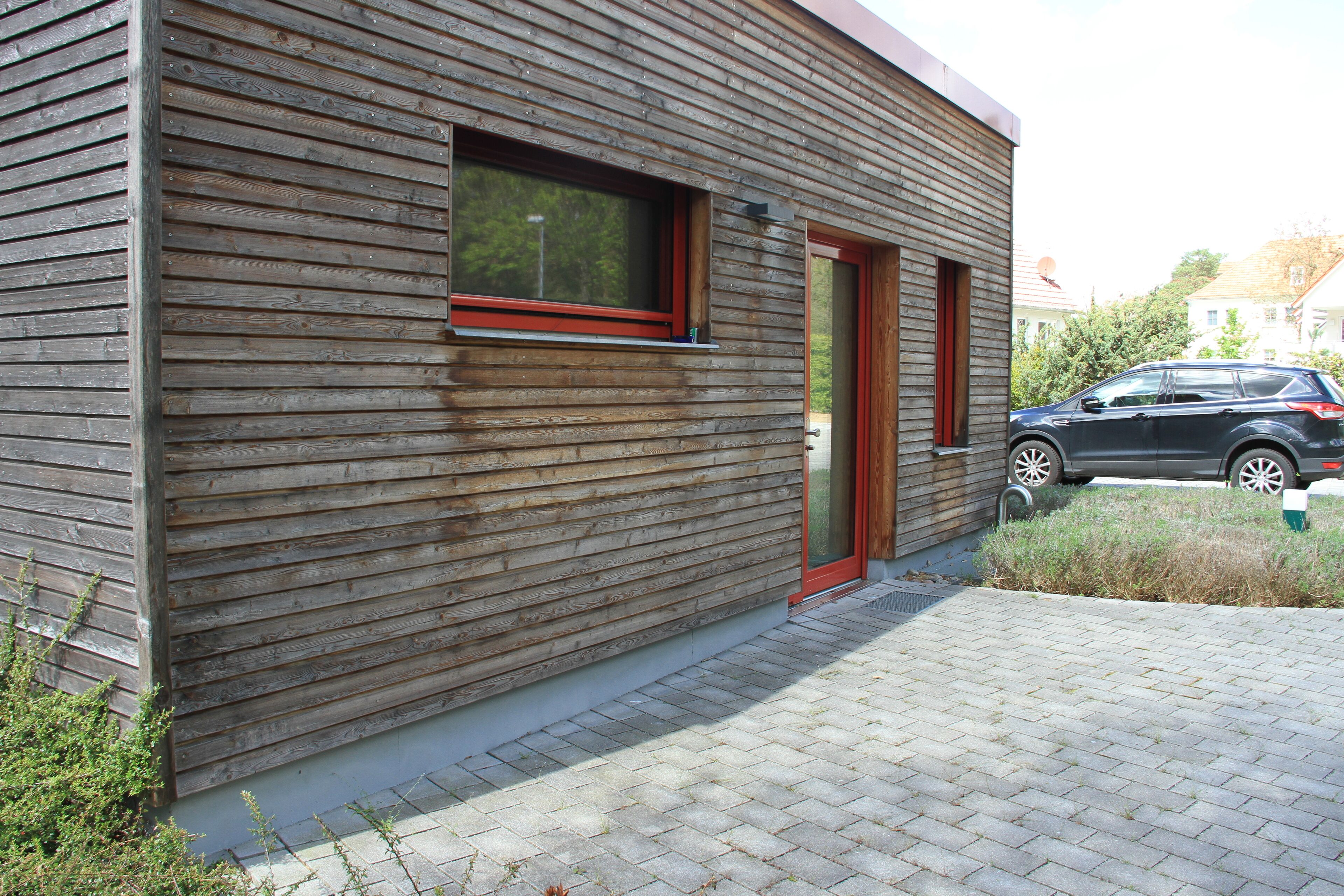A modern building with horizontal wooden siding, a red-framed window, and a door.
