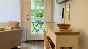 A living room with a sofa, a TV mounted on the wall, a wooden cabinet, and a door leading to an outdoor area. - Sleeps 9! Serene Sea Palms Golf Condo on St Simons|Close to Beach, Restaurants!  (St. Simons Island)